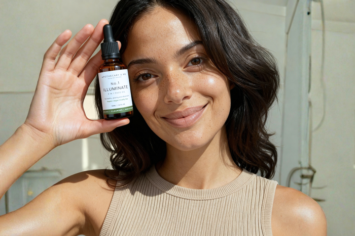  Woman with freckled, glowing skin smiling and holding a bottle of Apothecary & Me No.1 Illuminate Face Oil, a fragrance-free natural face oil for calming reactive and sensitive skin.